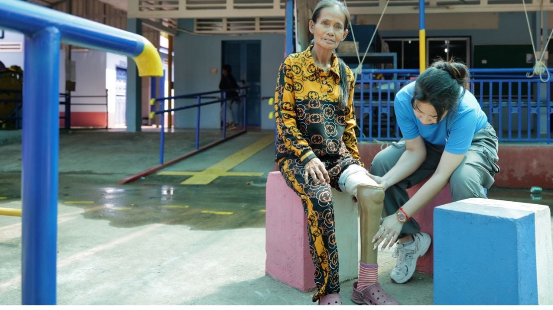 Een vrouw zit op een blok terwijl een kinesitherapeut haar beenprothese bekijket
